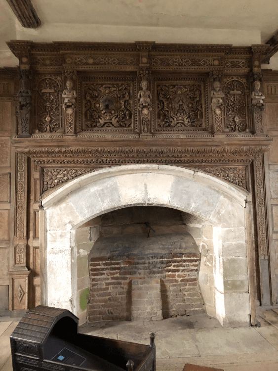 An ornate wooden mantlepiece around the stone fireplace within the castle